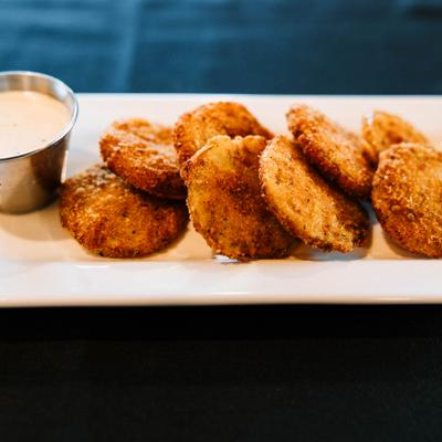 Fried green tomatoes served on a rectangular plate with a cup of creamy sauce.