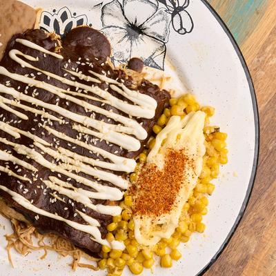 Enchiladas smothered in Mole sauce, sour cream, and sesame seeds, with rice, and beans.