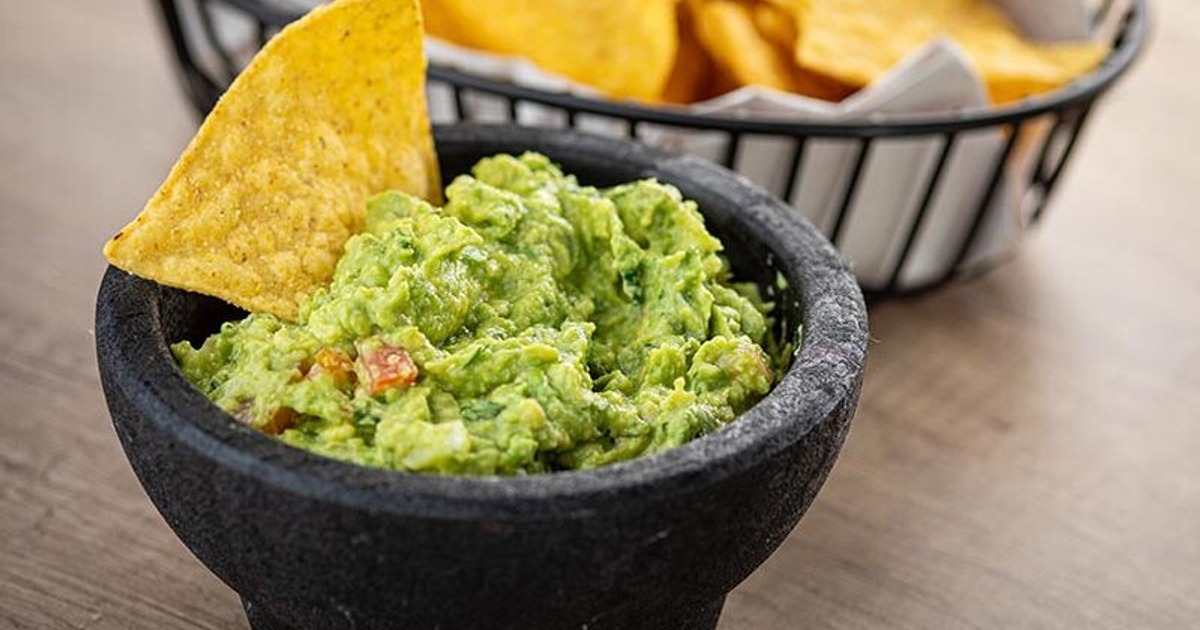 Guacamole in a stone bowl beside tortilla chips