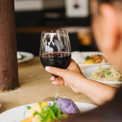 Person holding glass of red wine at the table.