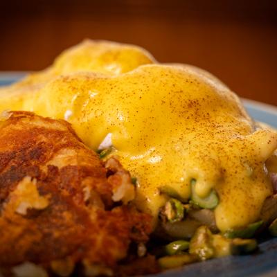 Classic eggs benedict served with crispy hashbrowns on plate.