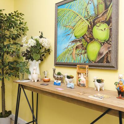 Wooden console table with decorative figurines beneath a colorful coconut painting.