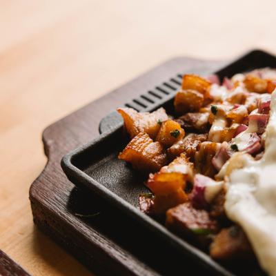 Close up view of sisig dish on hot plate with a fried egg.