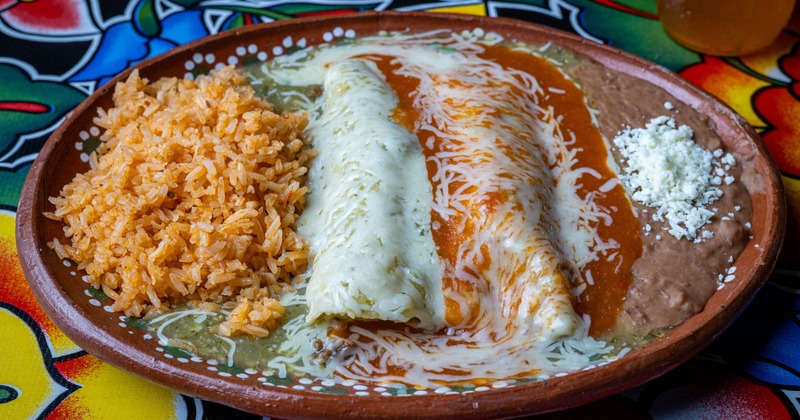 Enchilada plate with cheese and red sauces, orange rice, and refried beans