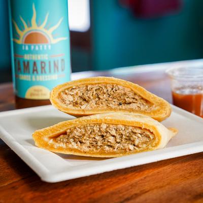 Jerk Chicken Patty cut in half, with a tamarind sauce bottle in the background.
