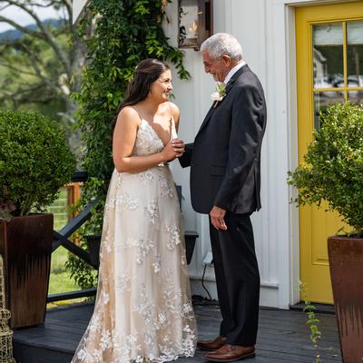A bride  smiles warmly while talking to a guest on a porch with greenery and a yellow door