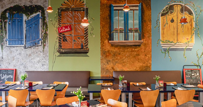 Banquette seating, tables and chairs by a wall decorated with mural