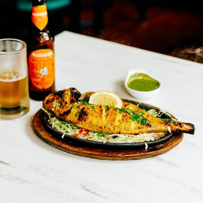 Whole snapper plate with a glass and bottle of beer.