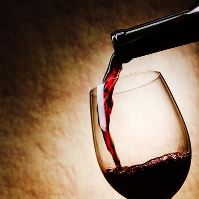 Red wine being poured into a glass in a dim lit setting.