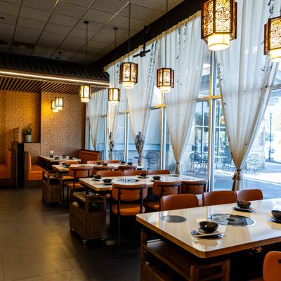 Interior featuring tables set for hot pot dining beneath distinct hanging light fixture.
