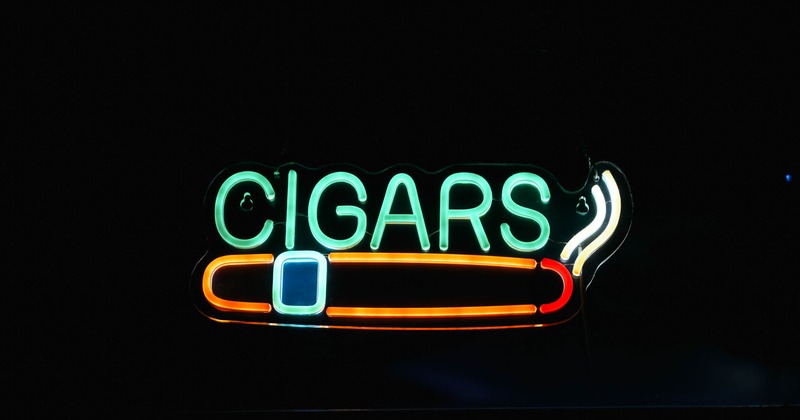 Neon sign featuring green lettering and an orange and red cigar outline