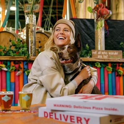 A person wearing a beige beanie hugging a brown dog in a vibrant cafe.