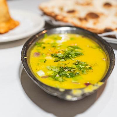 Yellow lentil curry garnished with cilantro, served with naan bread and samosa.