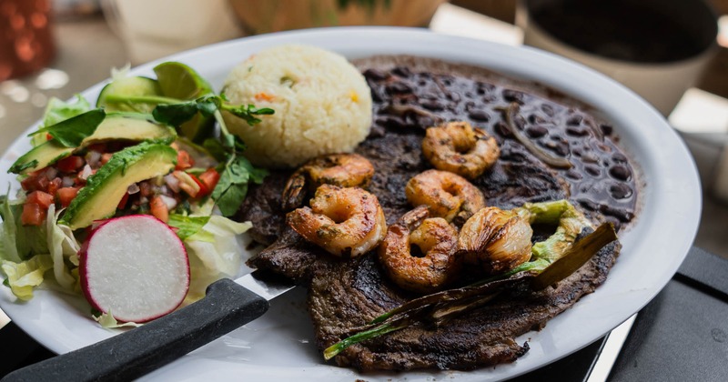 Carne asada served alongside shrimp, rice, a side salad, and tortillas