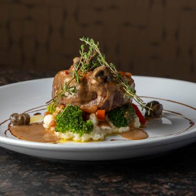 Plated gourmet meat served over mashed potatoes and broccoli.