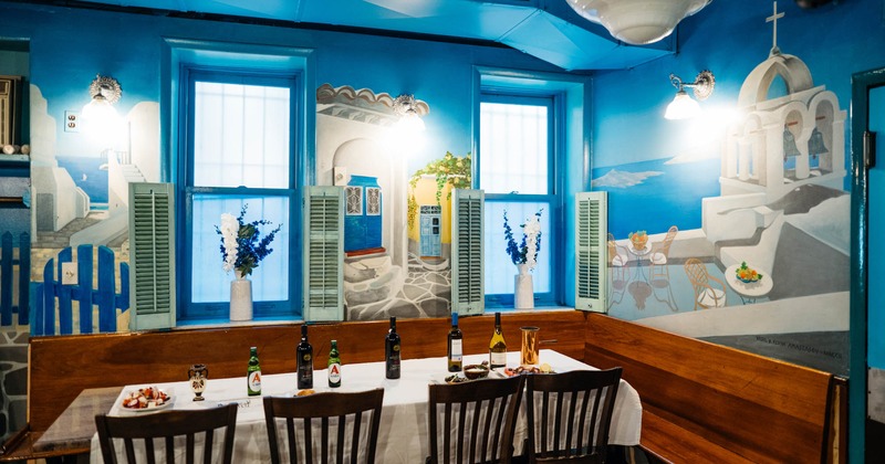 Interior, corner banquette bench with table and chairs, mural of Santorini on the walls