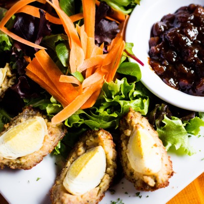 Scotch eggs quartered into slices on a plate with a green salad and a dish of pickled relish