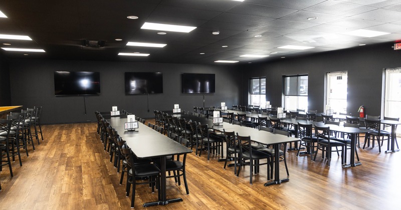 A spacious dining area with sleek black tables and chairs on a wooden floor