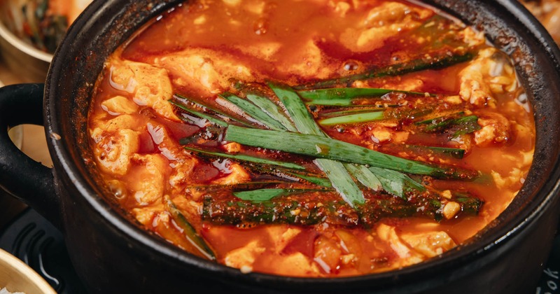 Spicy soft tofu stew garnished with green onion, close-up