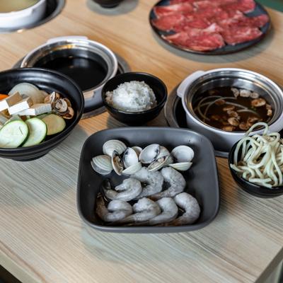 Side view of table spread, shrimp plate, various broth pots, rice and noodle cups.