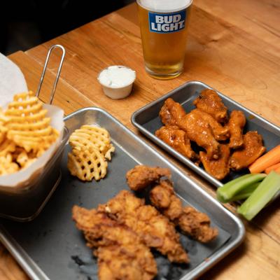 Chicken tenders with fries, chicken wings with celery and carrots, a glass of beer.