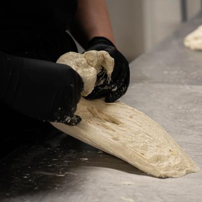 Gloved hands shaping a piece of dough on a metal counter.