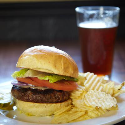 A burger with pickle, tomato, onion, lettuce and cheese, served with chips.