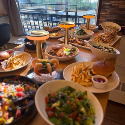 Colorful spread of various dishes with nachos, burgers, fries, and salads.