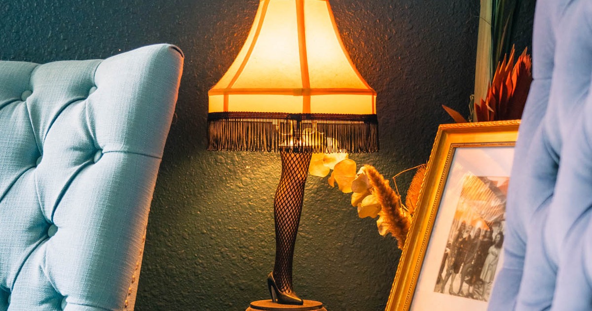 Nightstand lamp with a vintage, leggy design, next to a teal armchair and a framed picture