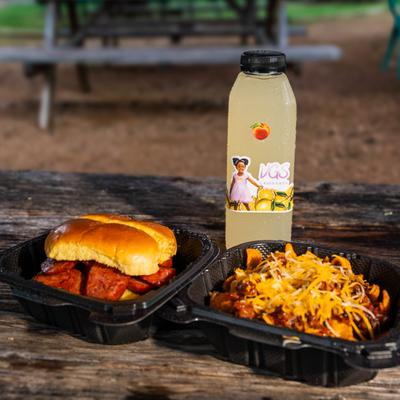 Barbecue sausage sandwich, Frito chili pie, and bottled lemonade on a picnic table.
