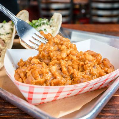 Fork with a bite of Boston Baked Beans, alongside tacos.