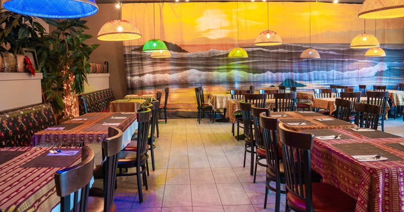 Interior of a restaurant with colorful tablecloths, pendant lights, and a seaside mural