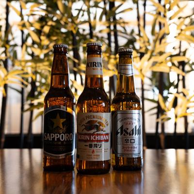 Three bottles of Japanese beer on a wooden counter against a leafy background.