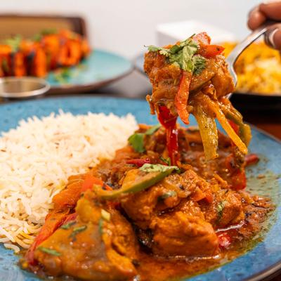 A fork holds chicken tikka masala over a blue plate with the dish and basmati rice.