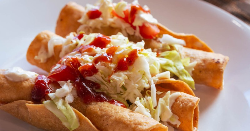 Crispy taquitos topped with cabbage slaw and salsa