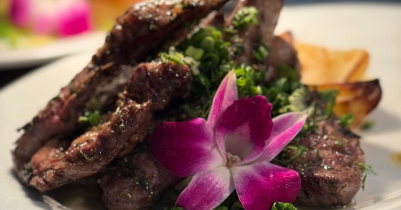 Three beef patties topped with microgreens, served next to two sauce dips