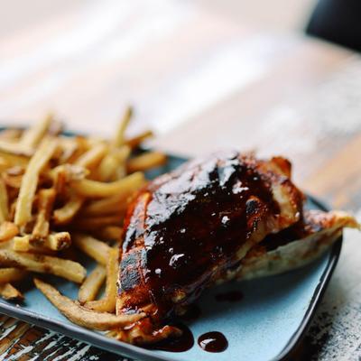 Barbecue chicken coated in rich sauce served with fries on a blue plate.