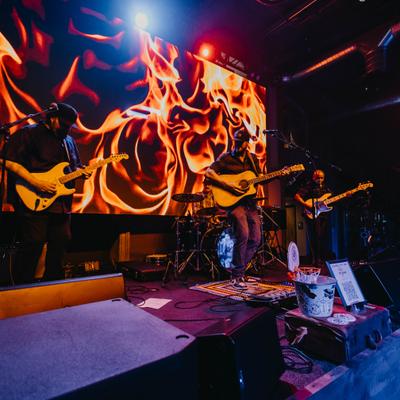 Live band playing with a large animated flame LED screen backdrop.