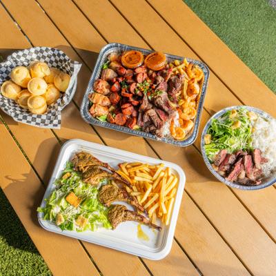 Grilled lamb chops, mixed meat platter, and Brazilian cheese bread served outdoors.