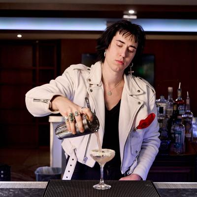 Bartender pouring cocktail into a coupe glass.