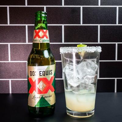 Mexican beer alongside a glass with ice, lime juice, and a salty rim.