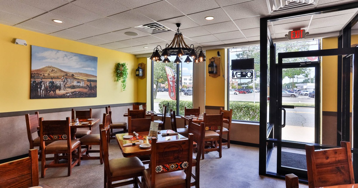Interior of a brightly lit restaurant with wooden tables and chairs, yellow walls, and large windows