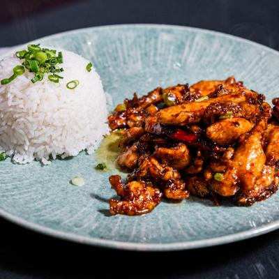 Stir fried chicken served with white rice on plate.