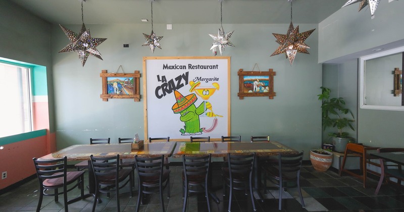 Interior of a Mexican restaurant with a long table, decorative lights, and a sign featuring a cactus character