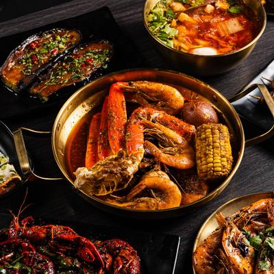 Vibrant food spread including seafood boil, crawfish, skewers, and a spicy soup.