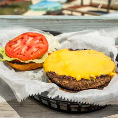 Cheeseburger topped with melted cheese, tomato, and lettuce served open-faced.