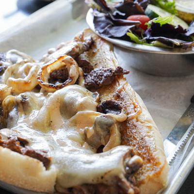 Grilled ribeye sandwich with mushrooms, onions, cheese, horseradish sauce, and side salad.