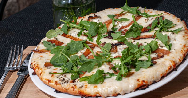 Home on the Farm Pizza with white sauce, caramelized onions, goat cheese, and arugula.