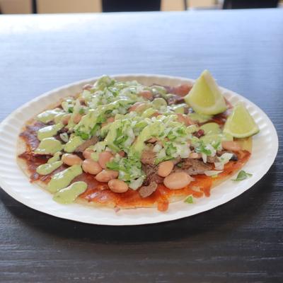 Steak taco with cheese, beans, sausage, avocado sauce, onion, and cilantro.