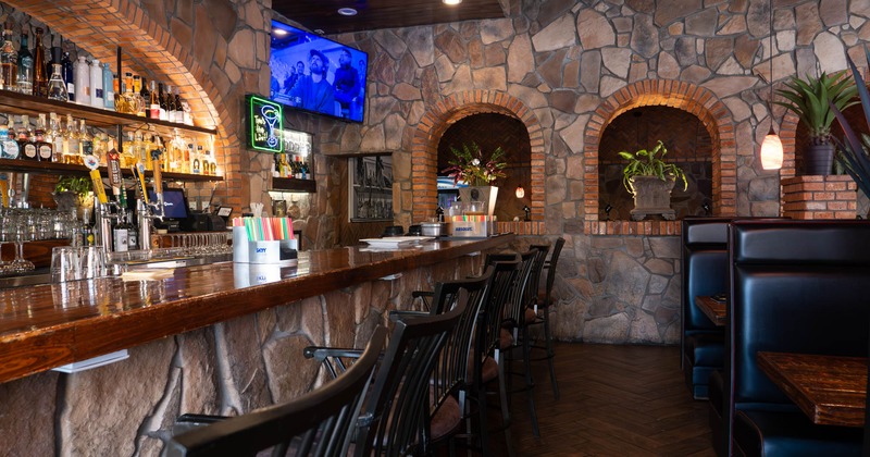 Interior, bar area, wooden top bar with stools, booths on the right, stone covered walls